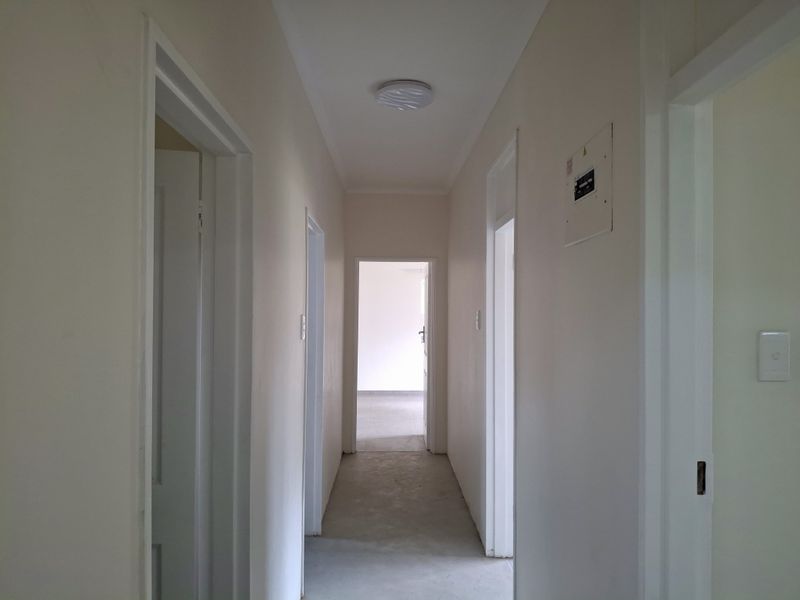 A clean, empty hallway featuring neutral walls, a ceiling light fixture, and an accessible electrical distribution board.