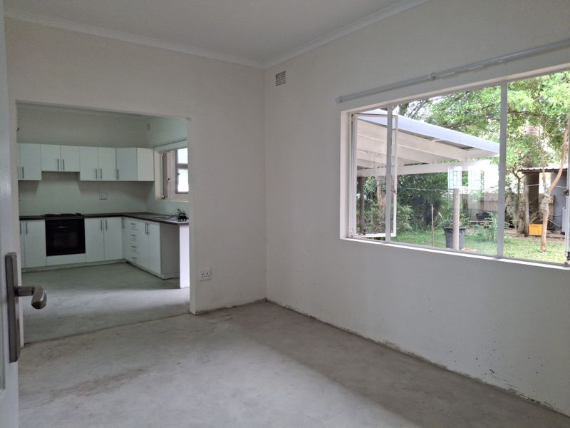 An open-plan living area featuring a connected kitchen with built-in cabinetry, oven, and hob, overlooking a rear garden through a large window.