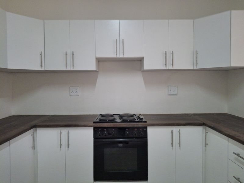 A clean, modern kitchen featuring white cabinetry, dark laminate countertops, and a built-in electric oven and hob.