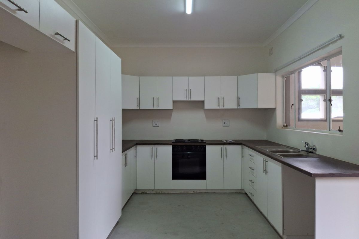 A functional kitchen featuring white cabinetry, dark countertops, a built-in oven and hob, and a double sink, awaiting final flooring and finishing touches.