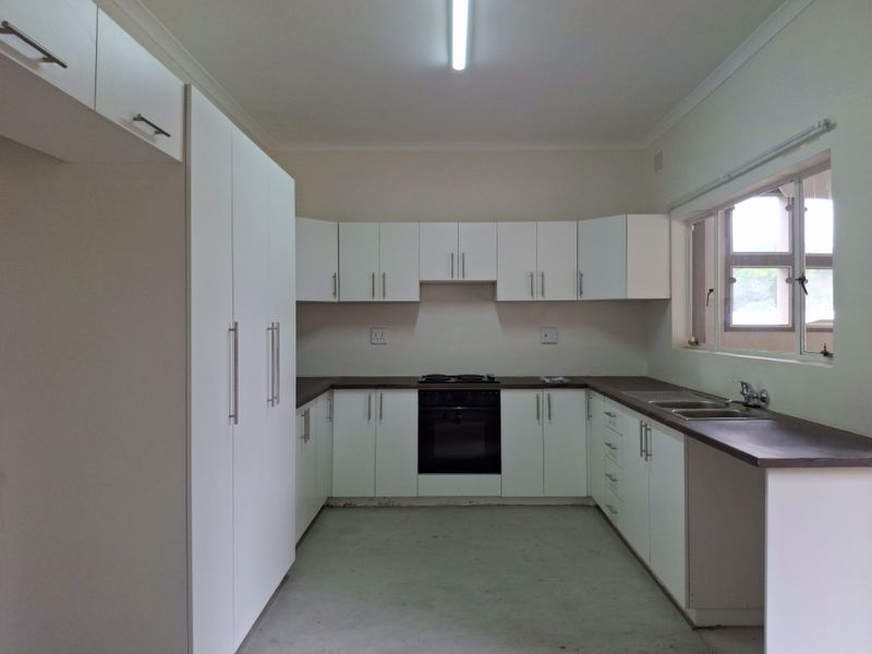 A functional kitchen featuring white cabinetry, dark countertops, a built-in oven and hob, and a double sink, awaiting final flooring and finishing touches.