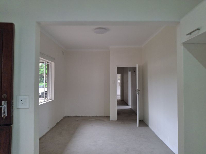 An empty, neutral-toned living area featuring a clean layout, internal door access, and an aluminium window, ready for flooring installation and interior finishing.
