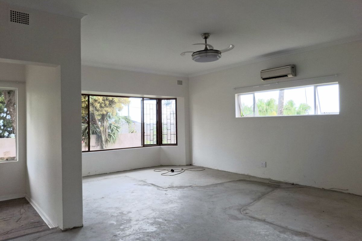An empty, open-plan living area featuring a ceiling fan, split-system air conditioning, and large bay windows, currently awaiting new flooring installation.