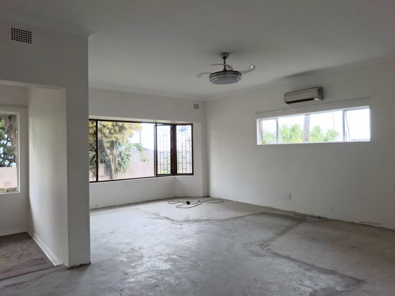An empty, open-plan living area featuring a ceiling fan, split-system air conditioning, and large bay windows, currently awaiting new flooring installation.