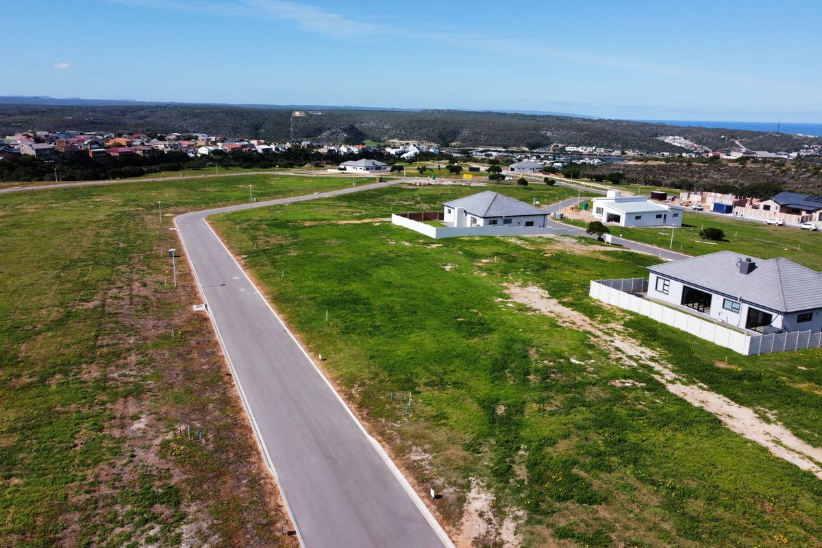 Aerial view of a residential development area featuring paved roads, open plots, and surrounding neighborhood infrastructure.