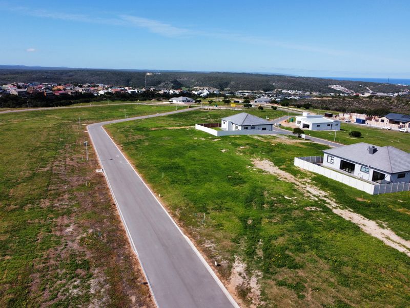 Aerial view of a residential development area featuring paved roads, open plots, and surrounding neighborhood infrastructure.