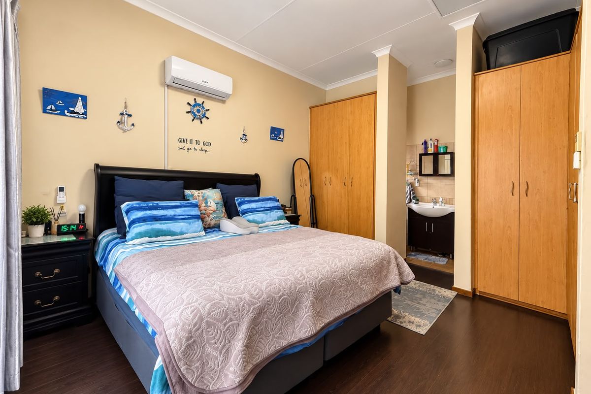 Spacious bedroom featuring laminate flooring, built-in wooden cupboards, a wall-mounted air conditioning unit, and a convenient open-plan en-suite vanity area.