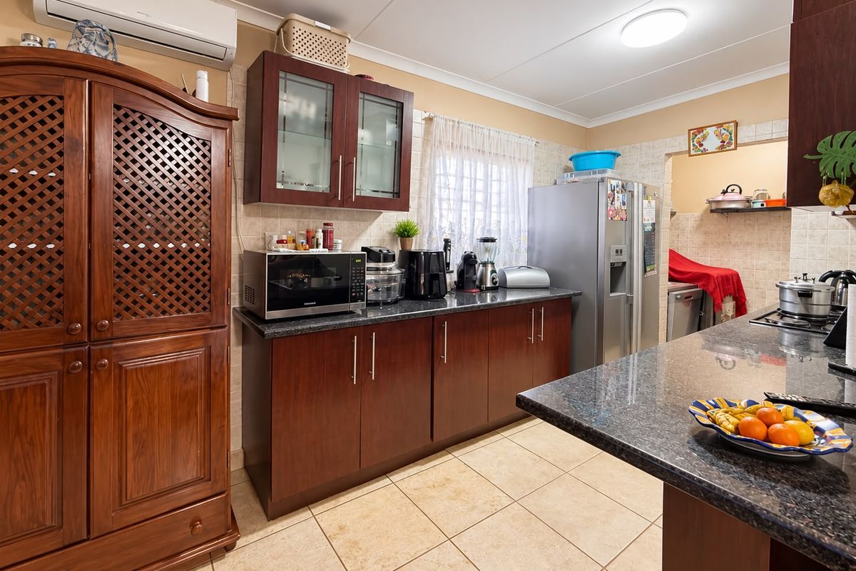 A functional kitchen featuring dark wood cabinetry, granite countertops, tiled backsplash, and ceramic flooring, with an adjacent scullery area visible.