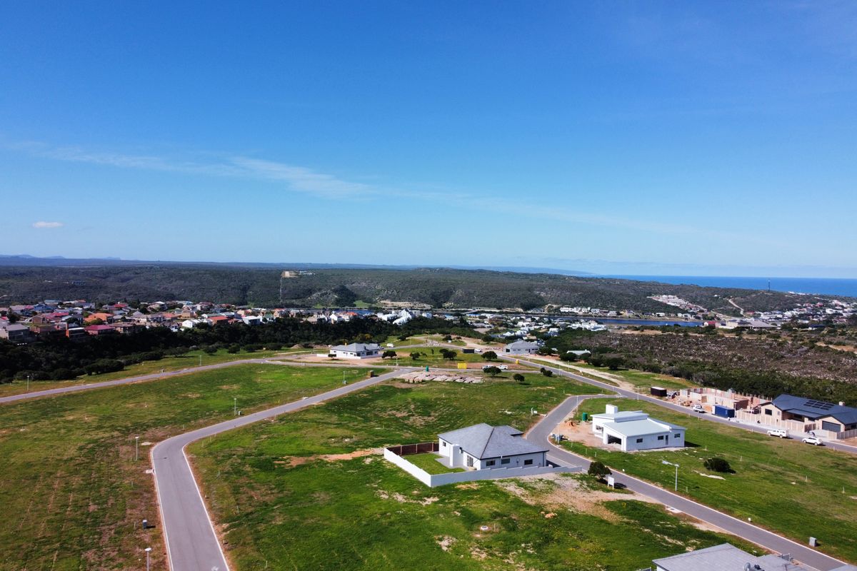 An aerial view of a residential development area featuring paved roads, established plots, and surrounding coastal landscape.