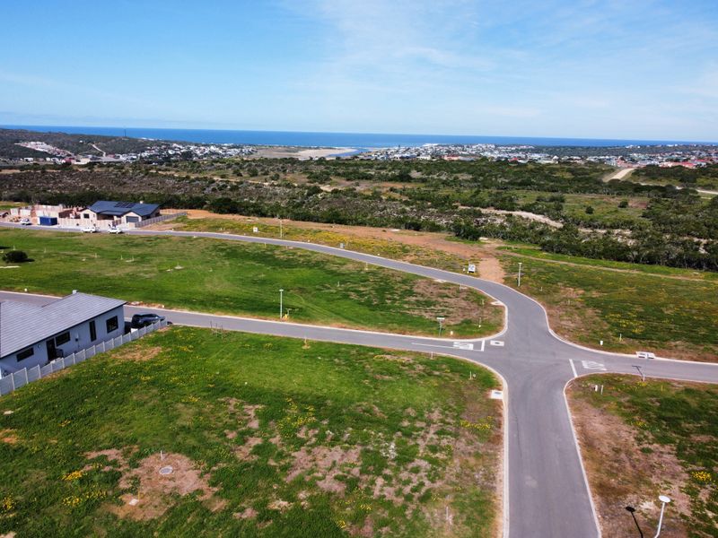 Aerial view of a residential development site featuring paved roads, street lighting, and expansive coastal views in the background.