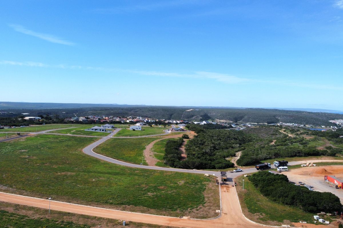 An aerial view of a residential development site featuring established paved roads, dirt access paths, and surrounding natural landscape.