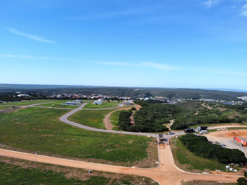 An aerial view of a residential development site featuring established paved roads, dirt access paths, and surrounding natural landscape.