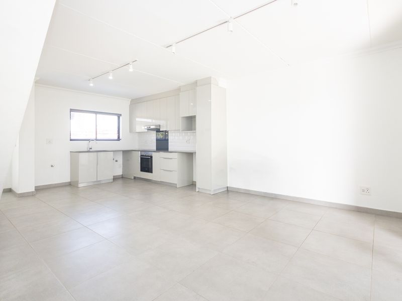 A bright, open-plan living and kitchen area featuring modern cabinetry, integrated appliances, neutral tiled flooring, and clean, minimalist finishes throughout.