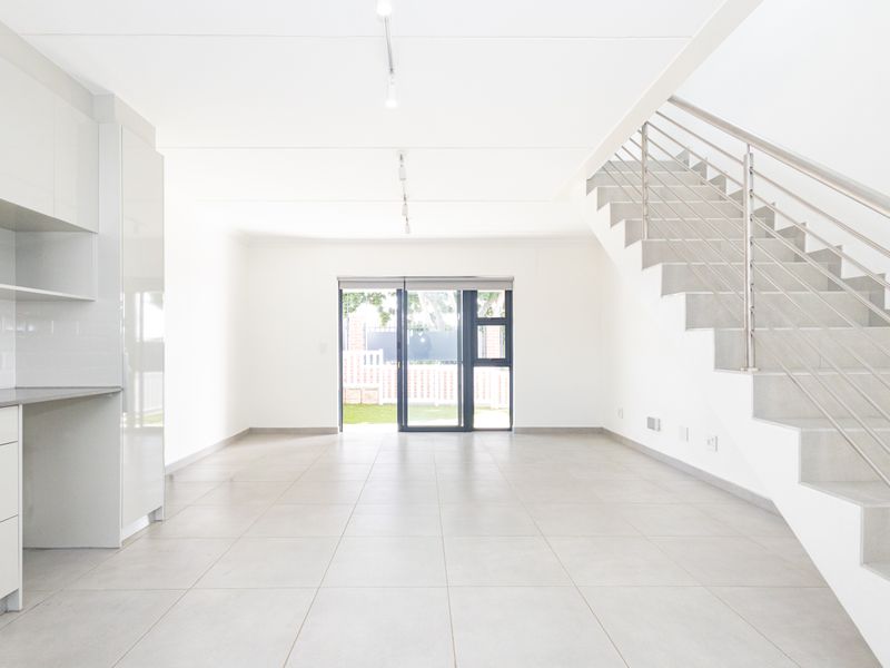 Bright and spacious open-plan living area featuring modern tiled floors, a sleek staircase with stainless steel railings, and a contemporary kitchen layout.