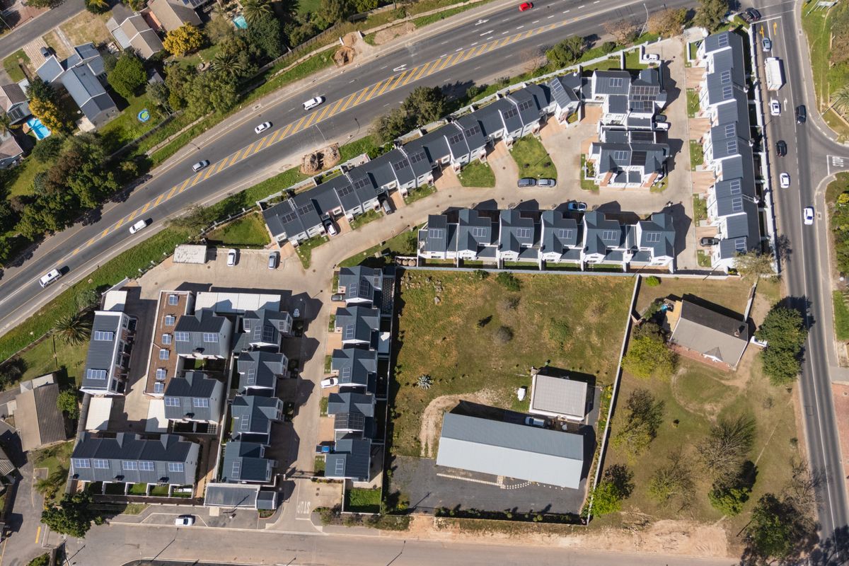 Aerial view of a townhouse complex featuring multiple residential units, paved access roads, and solar panel installations on rooftops.