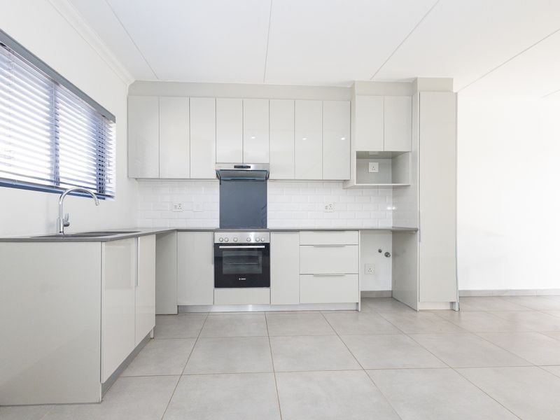 Modern, clean-lined kitchen featuring high-gloss cabinetry, subway tile backsplash, integrated oven, extractor fan, and neutral tiled flooring in an open-plan layout.