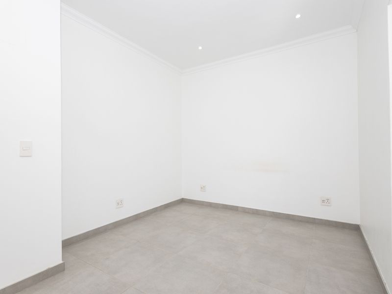 A clean, empty bedroom featuring neutral tiled flooring, recessed downlighting, and coving, providing a versatile blank canvas for interior design.