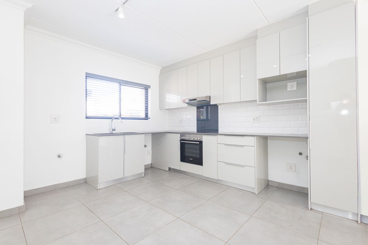 Modern, clean-lined kitchen featuring high-gloss cabinetry, subway tile backsplash, integrated oven, extractor fan, and neutral ceramic floor tiling.