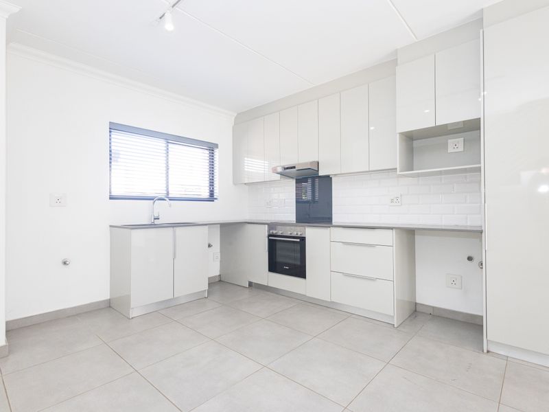Modern, clean-lined kitchen featuring high-gloss cabinetry, subway tile backsplash, integrated oven, extractor fan, and neutral ceramic floor tiling.