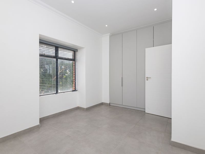 A bright, modern bedroom featuring neutral tiled flooring, built-in cupboards, and recessed downlights, offering a clean and versatile space.