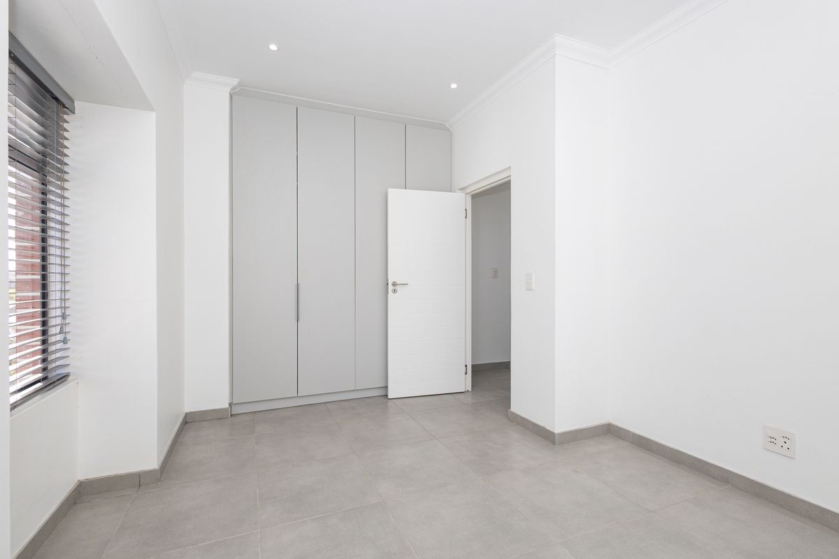 A bright, empty bedroom featuring neutral grey floor tiles, built-in cupboards, and modern recessed lighting.