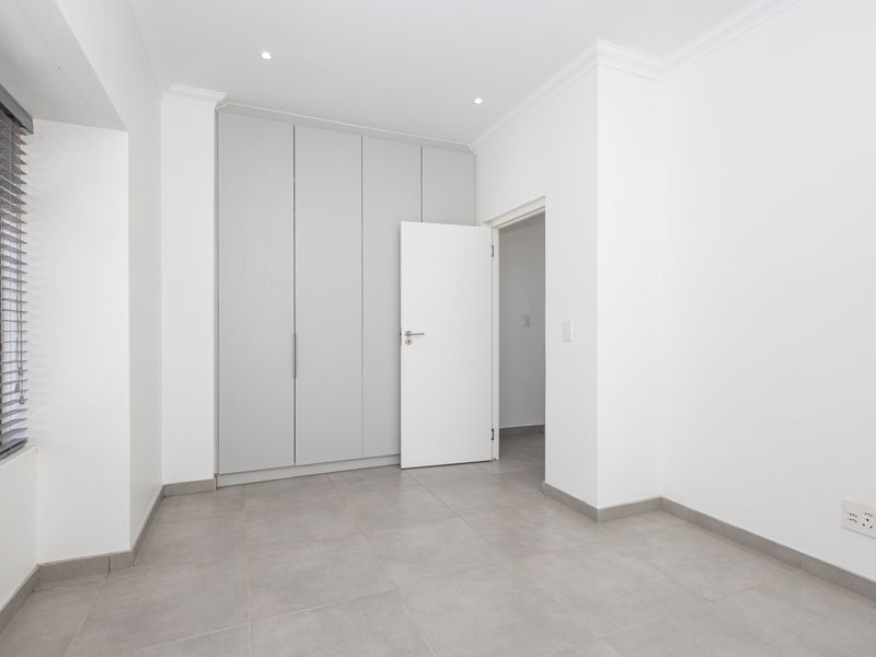 A bright, empty bedroom featuring neutral grey floor tiles, built-in cupboards, and modern recessed lighting.