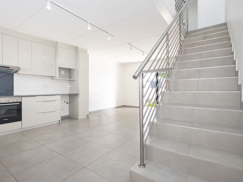Modern open-plan kitchen featuring sleek cabinetry, built-in appliances, and tiled flooring, adjacent to a staircase with a contemporary stainless steel balustrade.