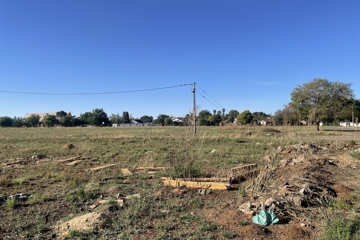 A vacant residential plot featuring open grass, uneven terrain, and an existing utility pole with overhead power lines.