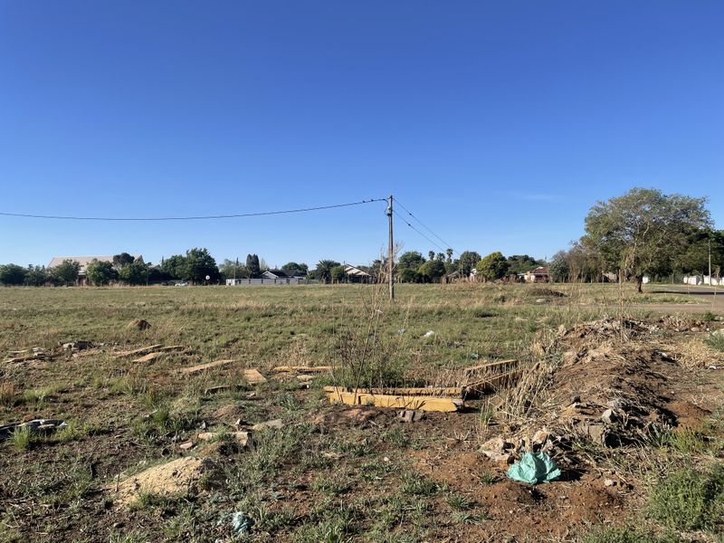 A vacant residential plot featuring open grass, uneven terrain, and an existing utility pole with overhead power lines.