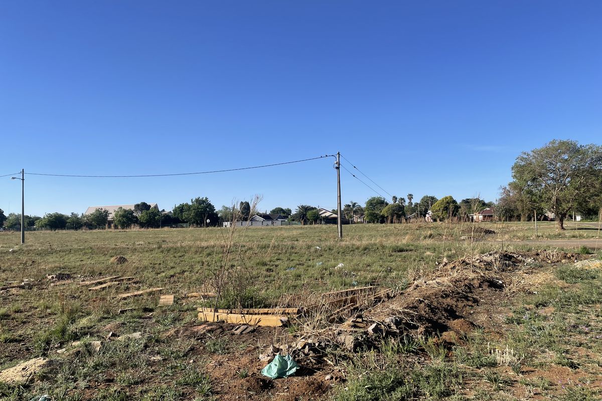 A vacant residential plot featuring open grass, uneven terrain, and existing utility infrastructure, suitable for future development.