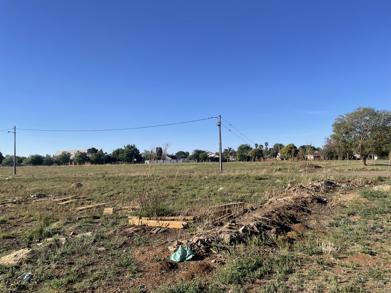A vacant residential plot featuring open grass, uneven terrain, and existing utility infrastructure, suitable for future development.
