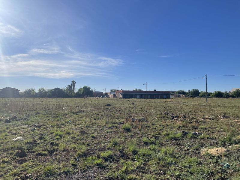 A wide-angle view of a vacant residential plot featuring open grass terrain with utility poles and power lines visible in the background.