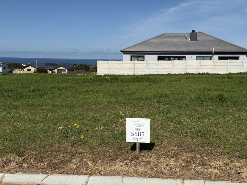 A vacant residential plot of 600 square meters featuring a level grass surface and a concrete boundary wall, with distant ocean views.
