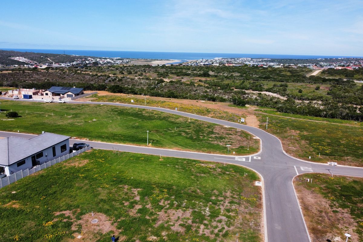 Aerial view of a residential vacant land development featuring paved roads, street lighting, and surrounding coastal landscape views.