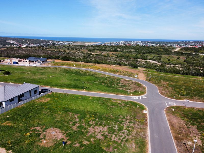 Aerial view of a residential vacant land development featuring paved roads, street lighting, and surrounding coastal landscape views.