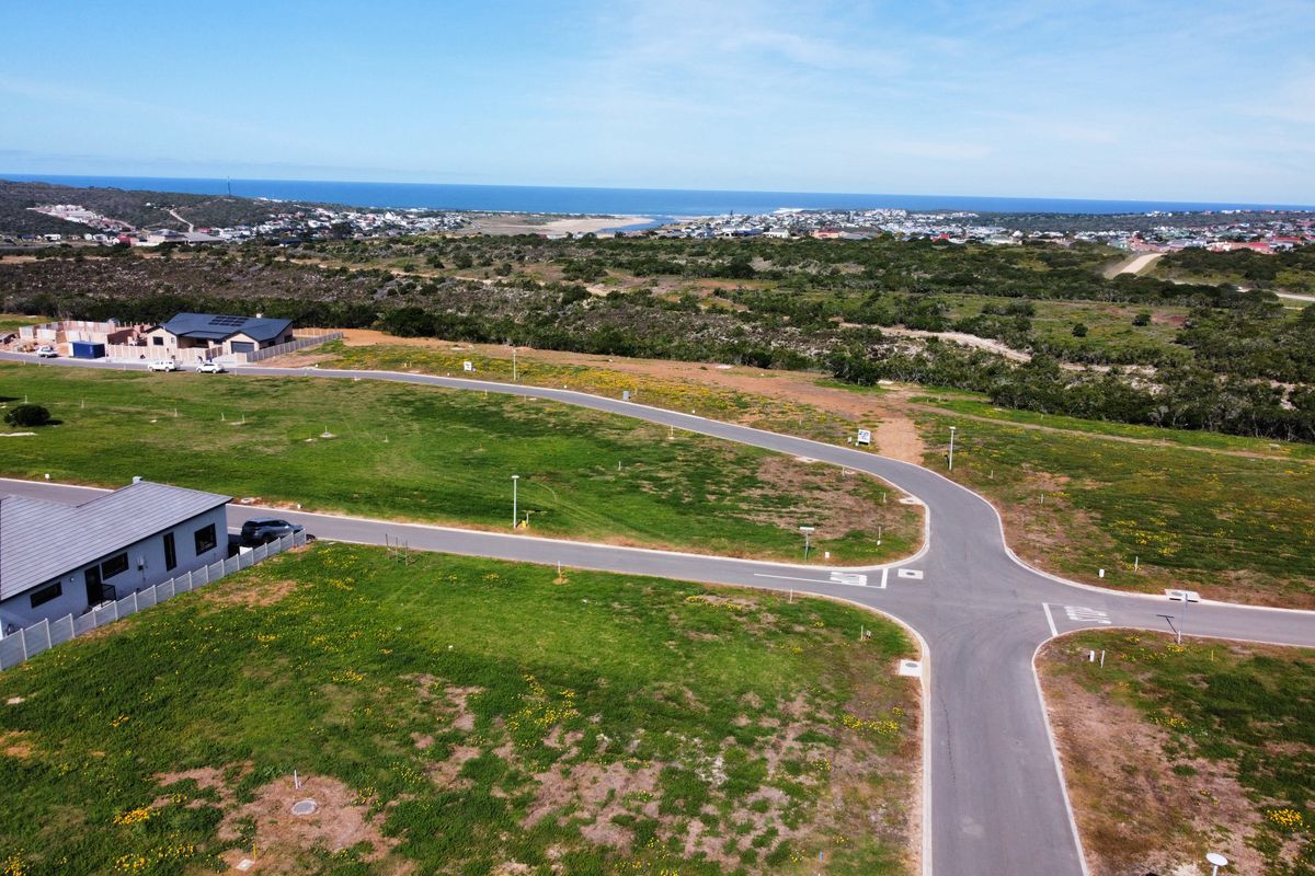 Aerial view of a residential development site featuring paved roads, street lighting, and expansive coastal views in the background.