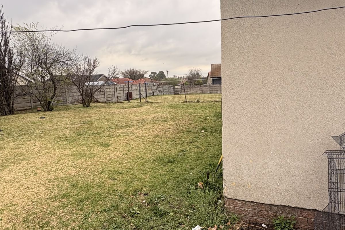 A view of the rear garden area featuring a grass lawn and concrete boundary wall, adjacent to the side of the house.
