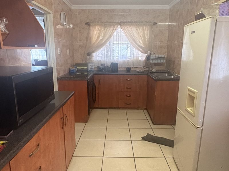 A functional kitchen featuring wooden cabinetry, tiled backsplash, and tiled flooring, offering a practical layout with ample storage space.