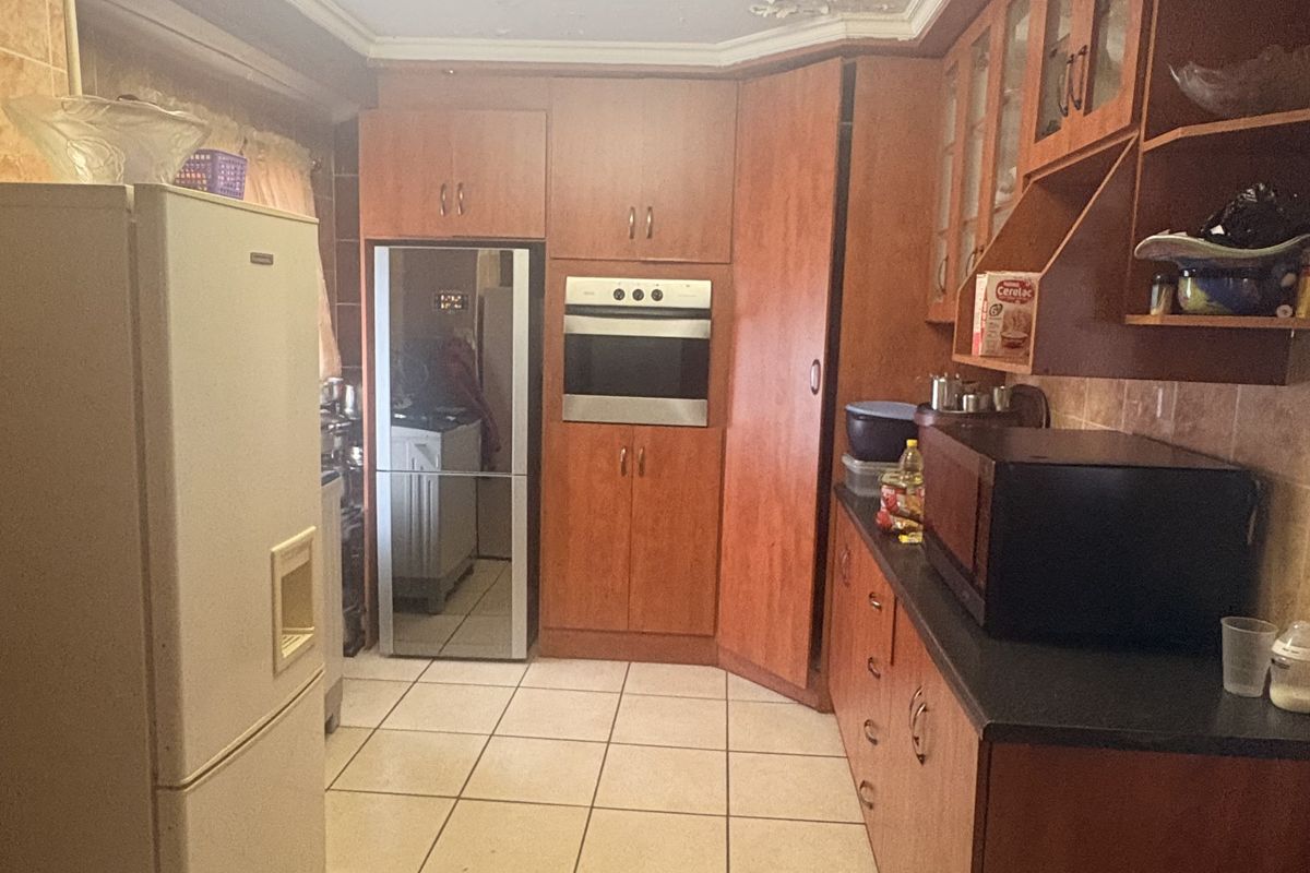 A dated kitchen featuring wood-finish cabinetry, built-in oven, and tiled flooring, currently showing signs of ceiling water damage requiring repair.
