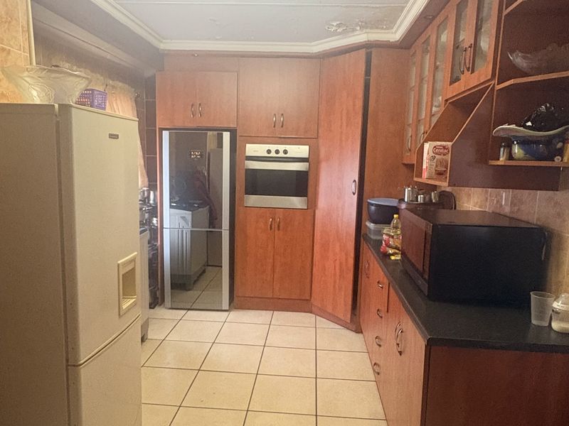 A dated kitchen featuring wood-finish cabinetry, built-in oven, and tiled flooring, currently showing signs of ceiling water damage requiring repair.