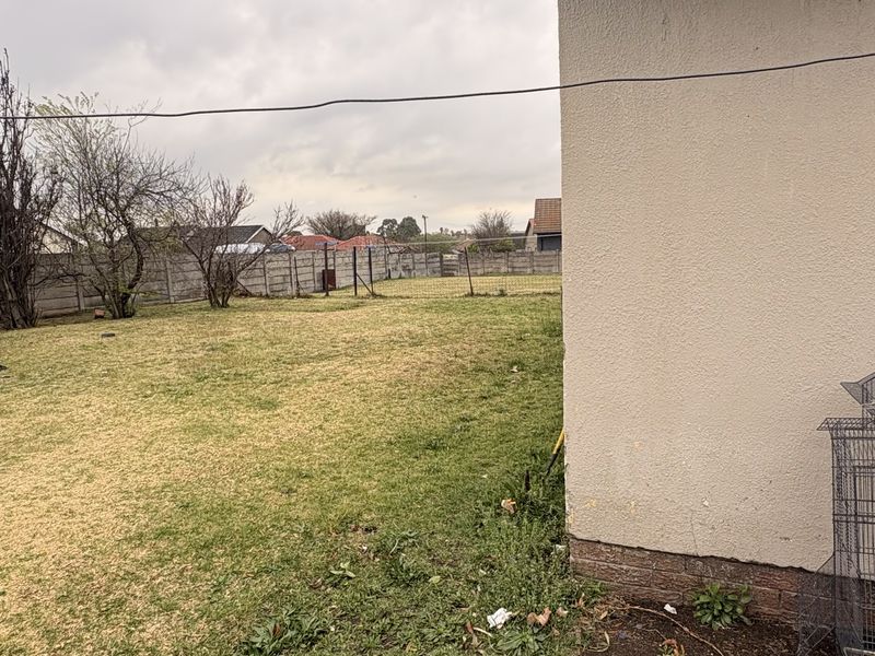 A view of the rear garden area featuring a grass lawn and concrete boundary wall, adjacent to the side of the house.