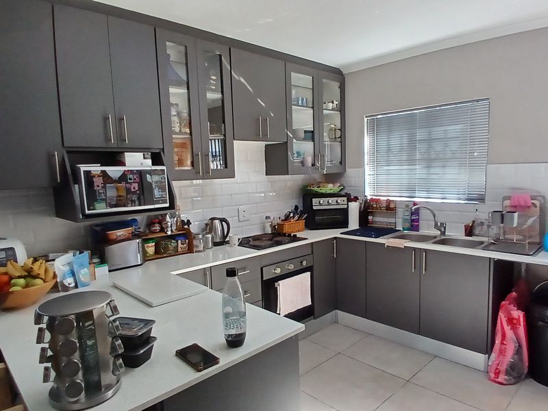 Modern kitchen featuring dark grey cabinetry, white subway tile backsplash, stone countertops, and integrated appliances in a functional U-shaped layout.