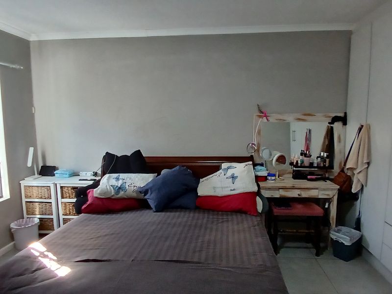 A functional bedroom featuring built-in cupboards, tiled flooring, and a window fitted with a security gate.