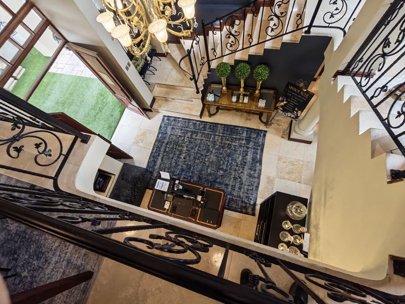 Grand double-volume entrance hall featuring elegant wrought iron staircase railings, stone tile flooring, and a decorative chandelier, with direct access to the garden.
