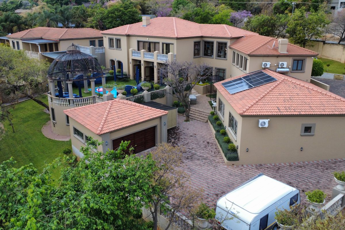 Aerial view of a large residential property featuring a terracotta tiled roof, solar panels, paved driveway, garage, and a landscaped garden with a gazebo.