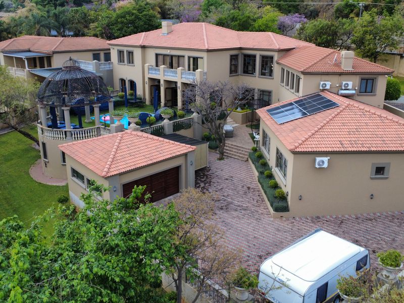 Aerial view of a large residential property featuring a terracotta tiled roof, solar panels, paved driveway, garage, and a landscaped garden with a gazebo.