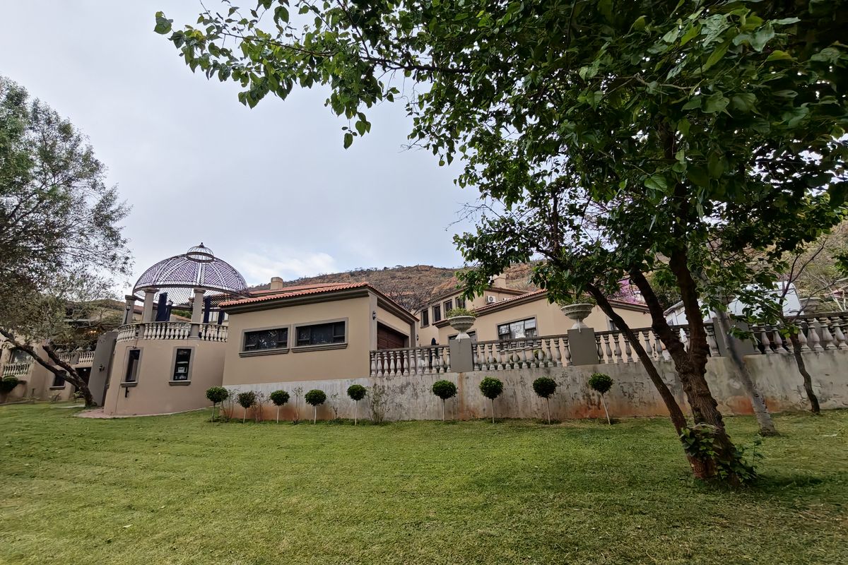 Rear view of the property featuring a landscaped garden, elevated terrace with balustrades, and a decorative gazebo structure.