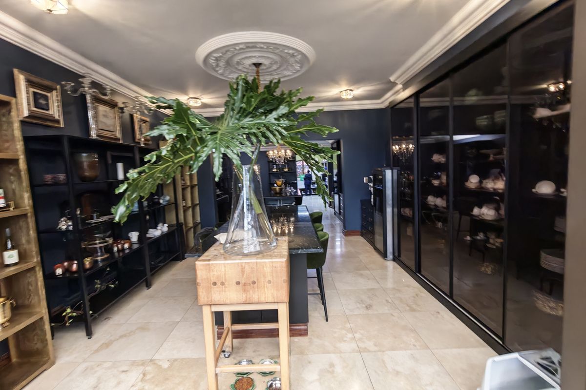 A sophisticated kitchen featuring a central stone island, dark cabinetry, elegant ceiling roses, and polished tiled flooring, creating a refined and functional culinary space.
