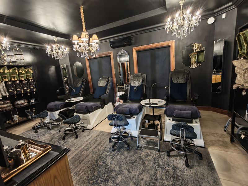 A professionally styled commercial space featuring dark walls, crystal chandeliers, and built-in shelving, currently configured as a salon or spa area.