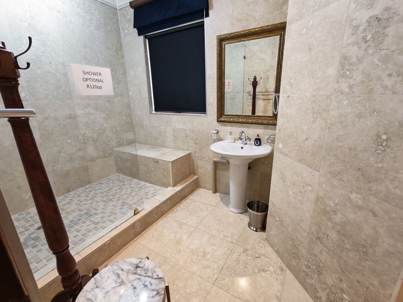 A well-maintained bathroom featuring travertine wall and floor tiles, a pedestal washbasin, and a spacious walk-in shower with a built-in bench.